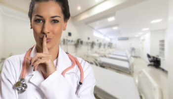 Serious doctor woman making silence sign over hospital corridor.